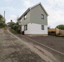 A house with grey siding and white lower walls next to a steep gravel road at Sevenwoods View in Longhope