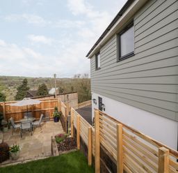 An outdoor patio with table chairs and umbrella next to a house with hill views at Sevenwoods View in Longhope