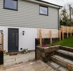 An exterior view of a house with a black door two wall lights a doormat and wooden steps leading to a grassy area at Sevenwoods View in Longhope