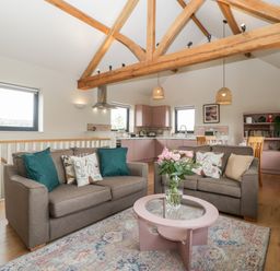 An open plan living room with two brown sofas a pink coffee table and a kitchen area with wooden beams at Sevenwoods View in Longhope