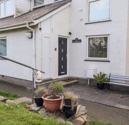 An exterior entrance of a white house with a black door and a bench with potted plants at The Summerhouse in Y Felinheli