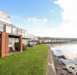 A waterfront property with a patio and glass balcony overlooking a body of water at The Summerhouse in Y Felinheli