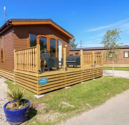 A wooden lodge with a deck and outdoor seating in a grassy area at Eden Lodge - Sherwood 21 in South Lakeland Leisure Village