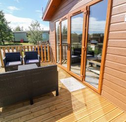 An outdoor wooden deck with black wicker seating and glass doors leading inside at Eden Lodge - Sherwood 21 in South Lakeland Leisure Village
