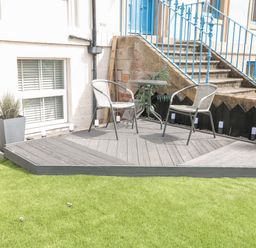 A small patio with two chairs and a round table on a wooden deck with potted plants and stairs in the background at Sunset View in Whitby