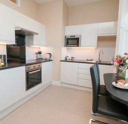 A kitchen with white cabinets black countertops a built-in oven microwave sink and a table with chairs and flowers at Sunset View in Whitby