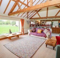 A living room with wooden beams cushions and rug next to a kitchen at The Lodge in Hickling near Catfield