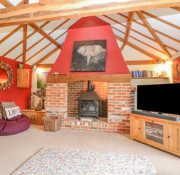 A living room with a brick fireplace wooden beams a television wooden cabinet and a bean bag at The Lodge in Hickling near Catfield