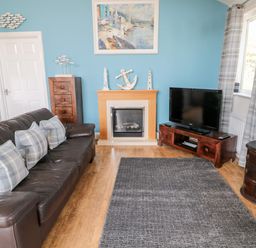 A living room with a leather sofa and cushions a fireplace a television and a rug at Sea View Lodge Eastfield Hall near Warkworth