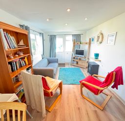 A living room with a bookshelf a sofa two chairs a rug and a TV at Trevone - Chalet 130 in St Merryn near Padstow