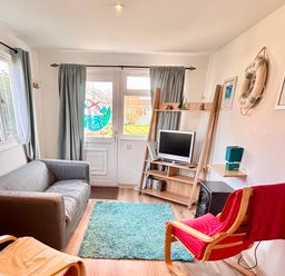 A living room with a grey sofa red chair wooden shelves and a small television at Trevone - Chalet 130 in St Merryn near Padstow