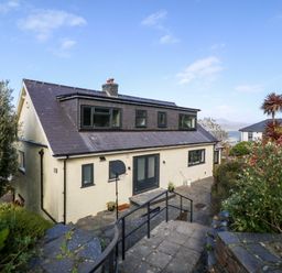 A two-story house with multiple windows and a basketball hoop by the entrance surrounded by greenery and a paved pathway at Machlud Haul in Llwyngwril