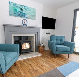A living room with two blue armchairs a fireplace with a wood-burning stove and a wall-mounted television at Machlud Haul in Llwyngwril