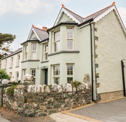 A stone-walled house with multiple windows and a paved driveway at Dolwern in Dinas Cross