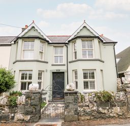 The front exterior of a semi detached house with bay windows and a stone wall at Dolwern in Dinas Cross