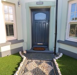 A front door with a doormat between two windows and pebble pathway at Dolwern in Dinas Cross