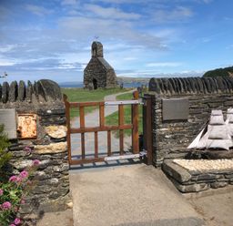 A stone gate with wooden gate leading to a stone building with a bell tower near the coast