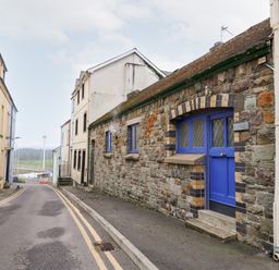 A narrow street with stone buildings and a blue door overlooking a river at Llys-Yr-Onnen in Carmarthen
