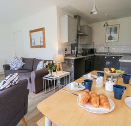 An open-plan kitchen and living area with a dining table set with croissants and cups at 17 Coedrath Park Saundersfoot