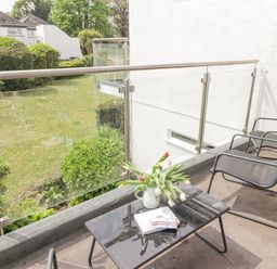 A balcony with two chairs and a table with a vase of flowers overlooking a garden at 28 Coedrath Park in Saundersfoot