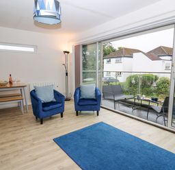 A living room with two blue armchairs a blue rug a dining table with benches and a patio with outdoor seating at 28 Coedrath Park Saundersfoot