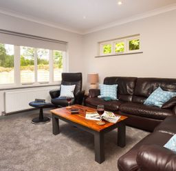A living room with brown leather sofas a wooden coffee table and large windows at Bellman Cottage in Bowness-On-Windermere