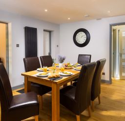 A dining room with a wooden table set for six with plates glasses and a centerpiece at Bellman Cottage in Bowness-On-Windermere