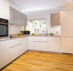 A kitchen with white cabinets wooden floor a microwave and an oven at Bellman Cottage in Bowness-On-Windermere