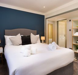A bedroom with a bed with pillows and rolled towels bedside tables with lamps and shelves with towels and decorative items at Bellman Cottage in Bowness-On-Windermere