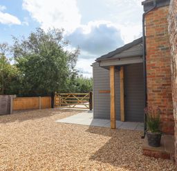 A gravel driveway with a wooden gate and a small porch attached to a brick and stone building at Bumblebee Cottage in East Nynehead near Bradford-On-Tone