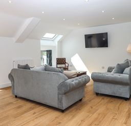 A living room with gray sofas a wooden chair a wall-mounted TV and wooden flooring at Bumblebee Cottage in East Nynehead near Bradford-On-Tone