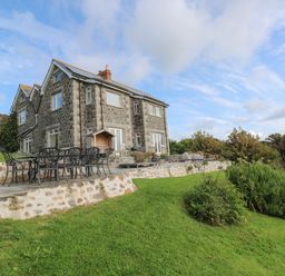 A stone house with a patio and outdoor dining set in a grassy garden at Penmarth House in Coverack