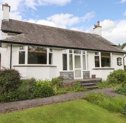 A front view of a single-story house with white exterior walls a tiled roof plants and shrubs in the garden at Halewood in Bowness-On-Windermere