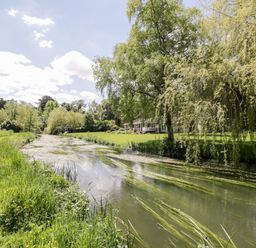 A river flowing through grass and trees with a house in the background at The River House Avon Valley Stonehenge with fishing Salisbury