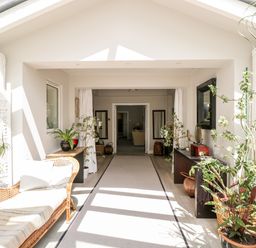 A sunlit hallway with plants a wicker bench and tables at The River House Avon Valley Stonehenge with fishing Salisbury