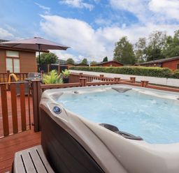 An outdoor hot tub on a wooden deck with patio furniture and umbrella at Black Dog Lodge Thirlmere 3 White Cross Bay near Windermere
