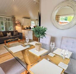A dining table set with placemats glasses and a plant next to a living room with a sofa and clock at Black Dog Lodge Thirlmere 3 White Cross Bay near Windermere