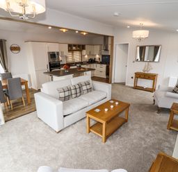A living room with a sofa and armchair a wooden coffee table and side tables an open kitchen and dining area with chairs at Bramblewick in Runswick Bay near Staithes