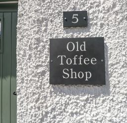 A textured white wall with a black house number 5 plate and Old Toffee Shop sign beside a green door at Old Toffee Shop in Ambleside