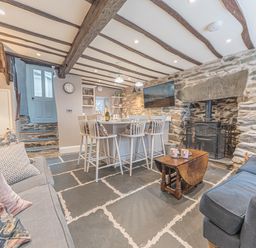 A living room with stone walls wooden beams a wood stove and a kitchen island with chairs at Old Toffee Shop Ambleside