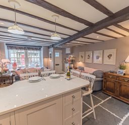 A kitchen island with plates and a bottle next to chairs in a room with exposed beams and stone walls at Old Toffee Shop in Ambleside