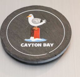 A circular coaster with a seagull standing on a red post and the words Cayton Bay