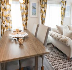 A dining table with chairs next to a sofa with cushions in a room with patterned curtains at The Rodley Pines in Cayton