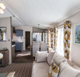An open plan living room and kitchen with a beige sofa dining table with chairs and yellow patterned curtains at The Rodley Pines in Cayton