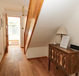 A hallway with wooden flooring a small wooden cabinet lamp and a few framed pictures at Rose Bank in Belford