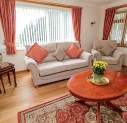 A living room with beige sofa and armchair orange cushions wooden side tables and round coffee table with a plant on a patterned rug at Rose Bank in Belford
