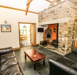 A living room with two black leather sofas a wooden coffee table and a stone fireplace with a wood burner at Trewrach Cottage in Dinas Cross