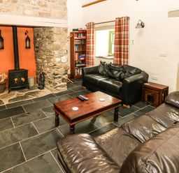 A living room with leather sofas a wood burning stove and a wooden coffee table at Trewrach Cottage Dinas Cross