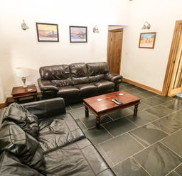 A living room with two leather sofas a wooden coffee table a side table with a lamp and three framed pictures on the wall at Trewrach Cottage in Dinas Cross