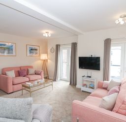 A living room with two pink sofas a grey armchair a glass coffee table a wall-mounted TV and two sets of French doors with curtains at Weydale Avenue in Scarborough
